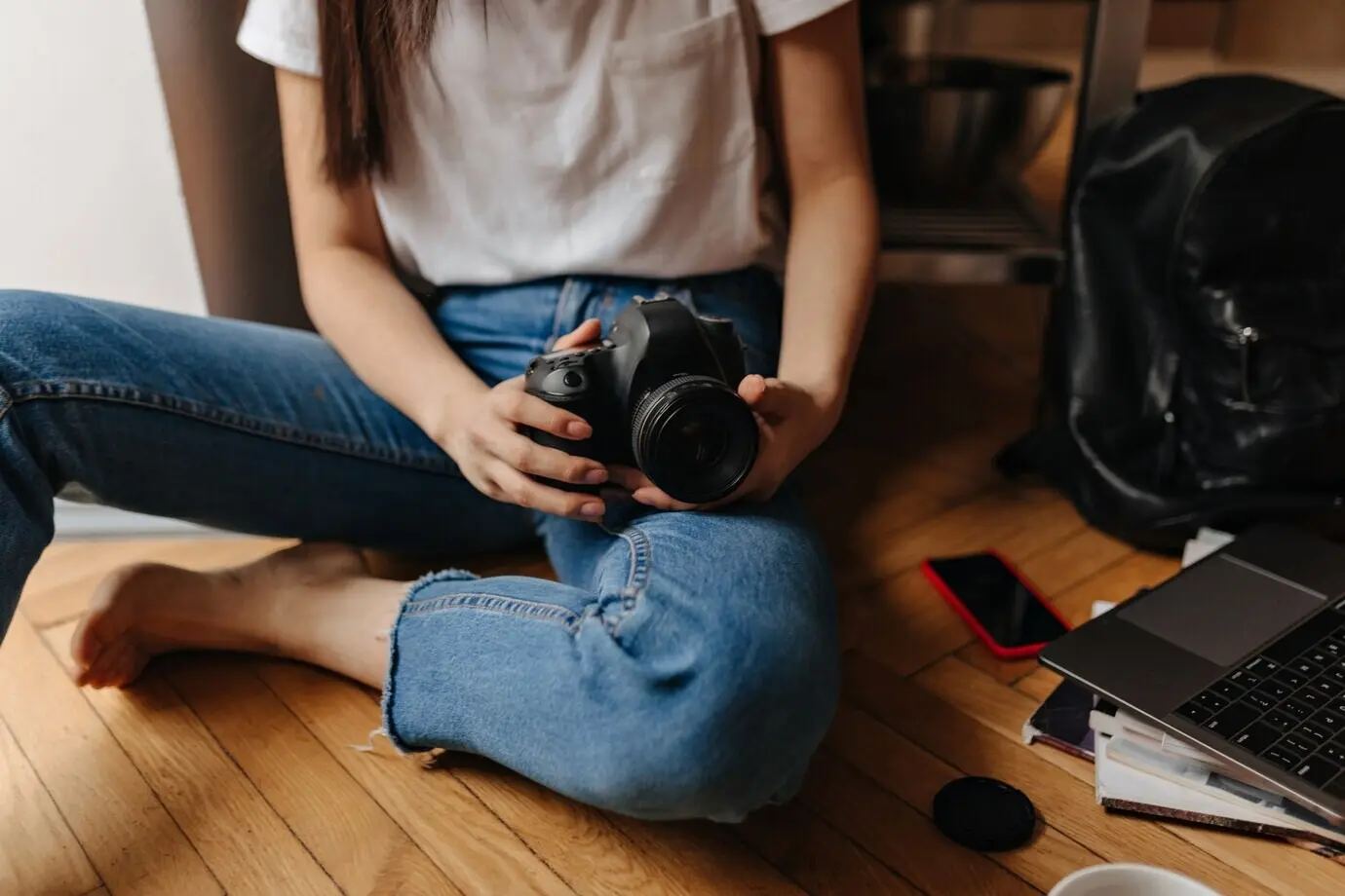 Photo of a woman in jeans sitting on the floor, front view, with a laptop and a phone.