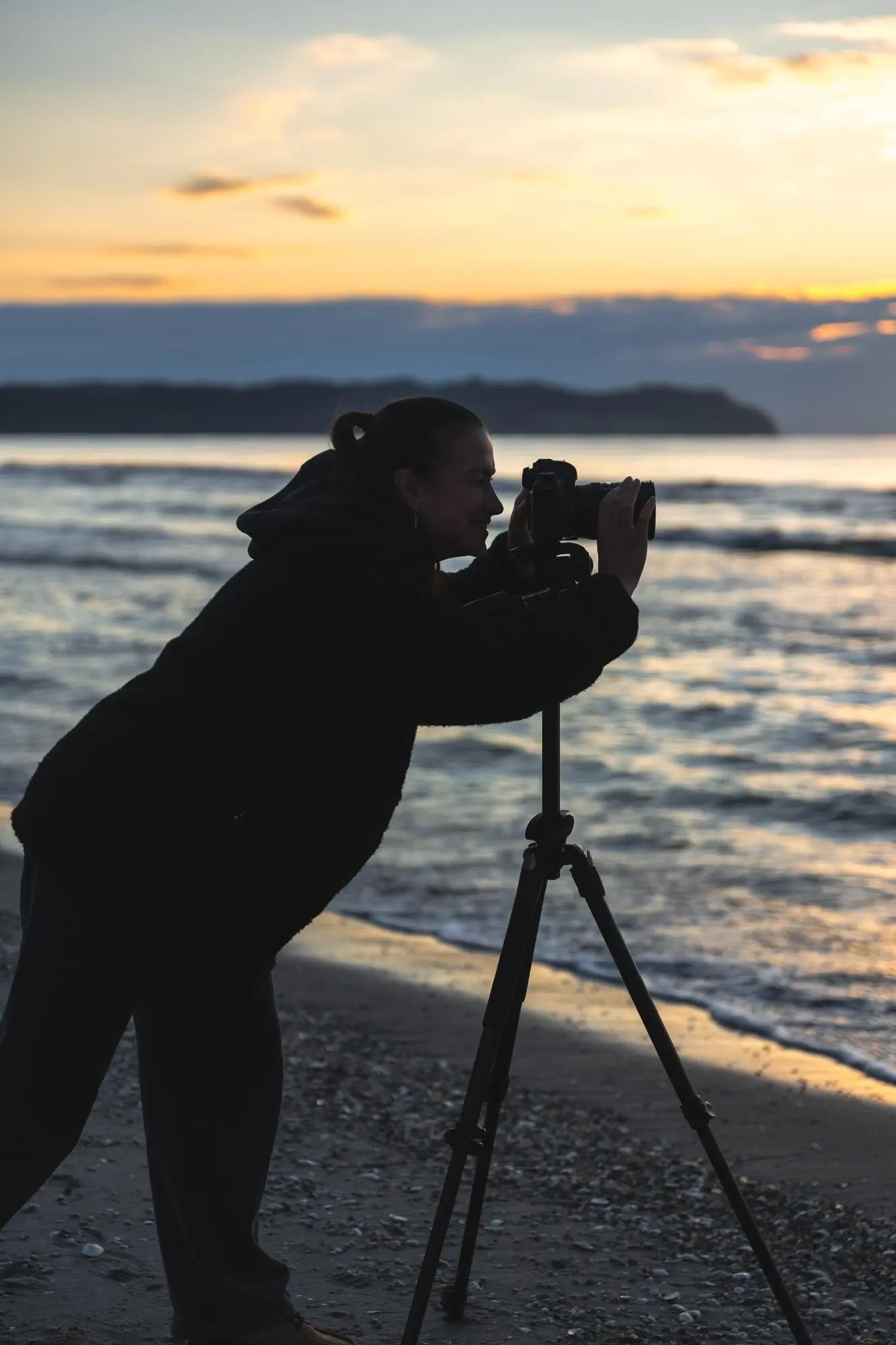 A woman photographer with a camera capturing the sunrise on the beach.