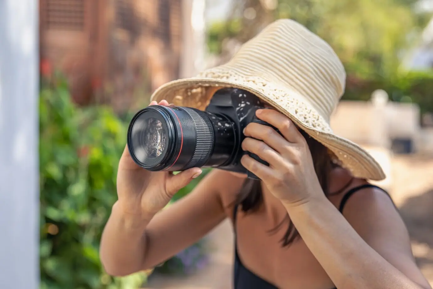 On a hot summer day, a young woman wearing a hat is taking photos with a professional SLR camera.
